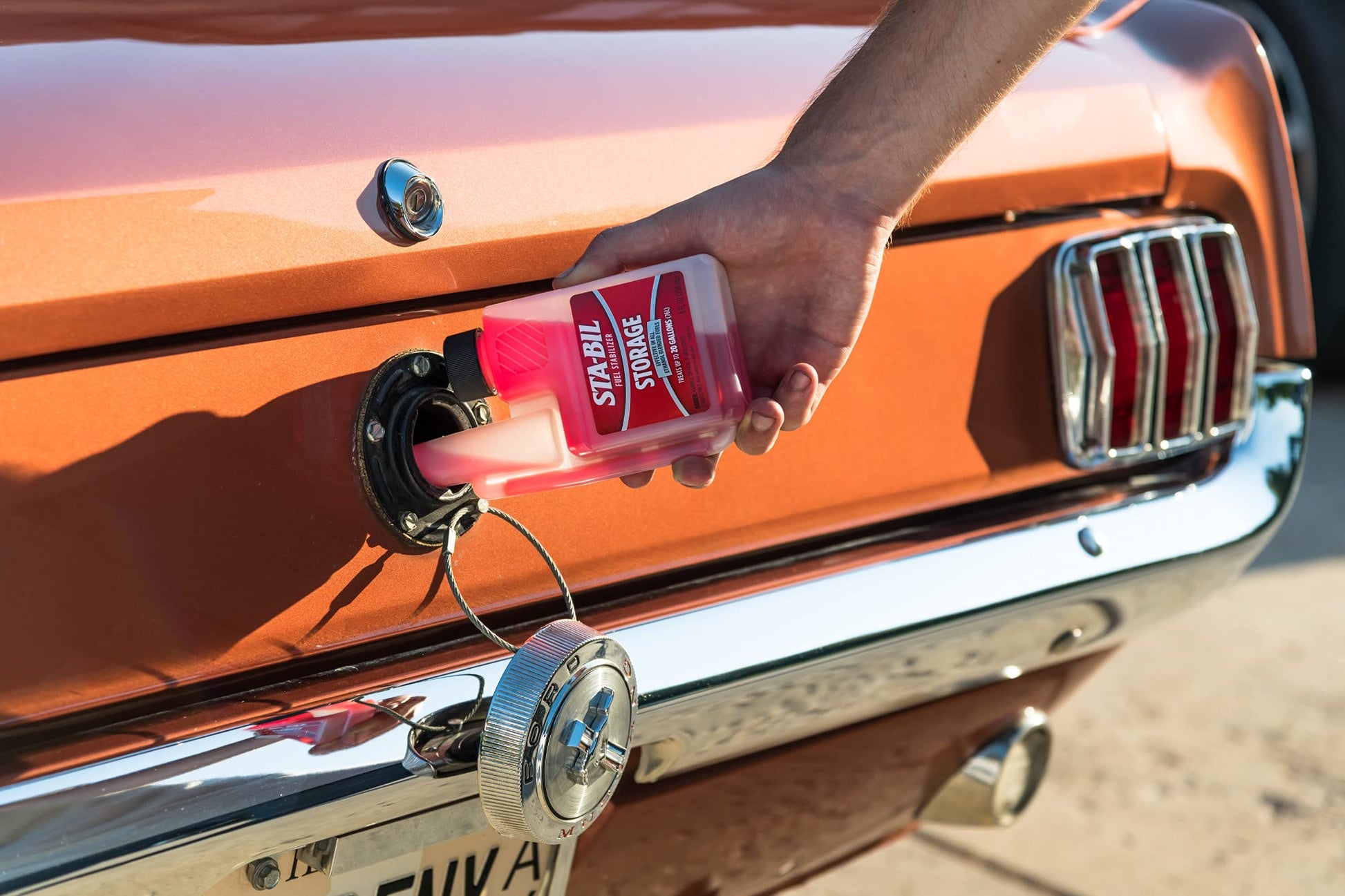 Person refueling a classic car with a red fuel canister.