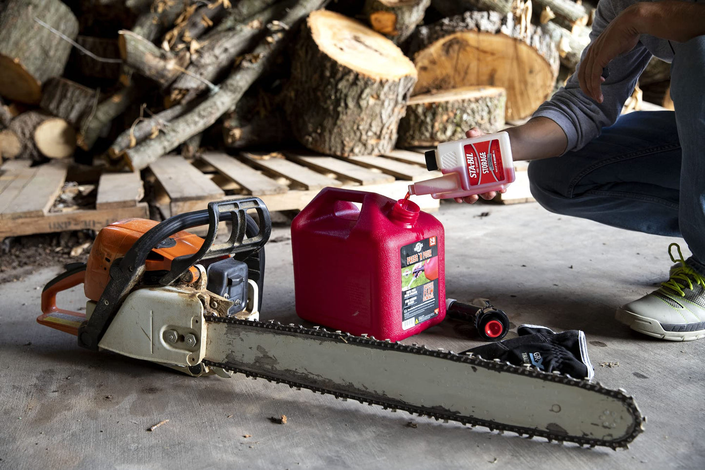 Chainsaw and gas canister on a concrete floor with stacked logs 