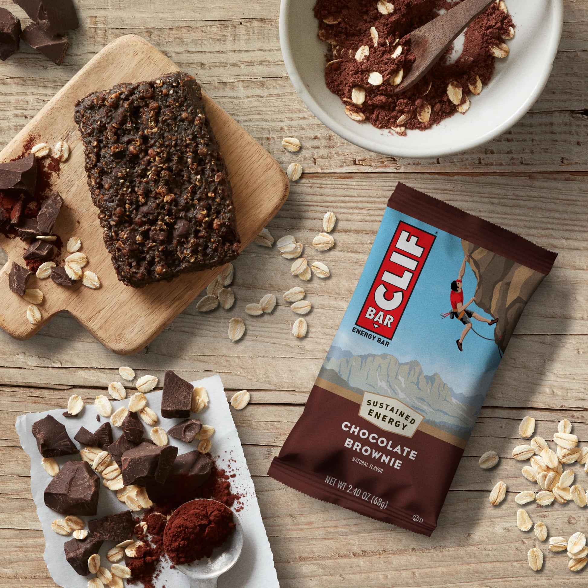 Clif Bar chocolate brownie energy bar on a wooden surface with ingredients and a loaf of bread.